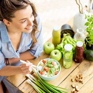 Woman eating salad at a table full of fruits and vegetables
