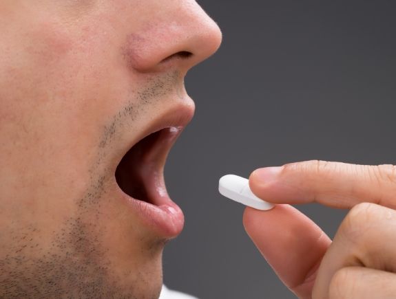 Man placing a white pill in his mouth
