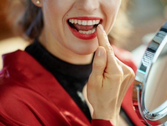 Woman with red lipstick looking at her smile in a mirror
