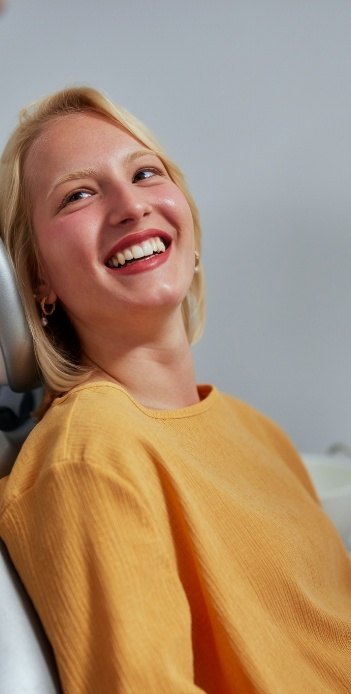 Woman in yellow sweater smiling while receiving dental services in West Caldwell