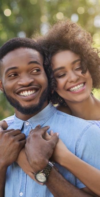 Young woman hugging young man in denim shirt from behind