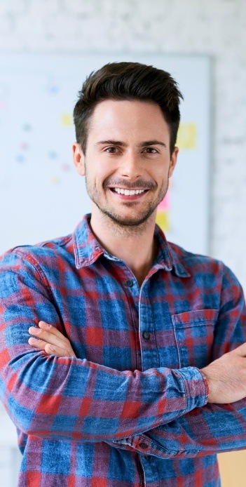 Smiling man in red and blue plaid shirt standing with arms crossed