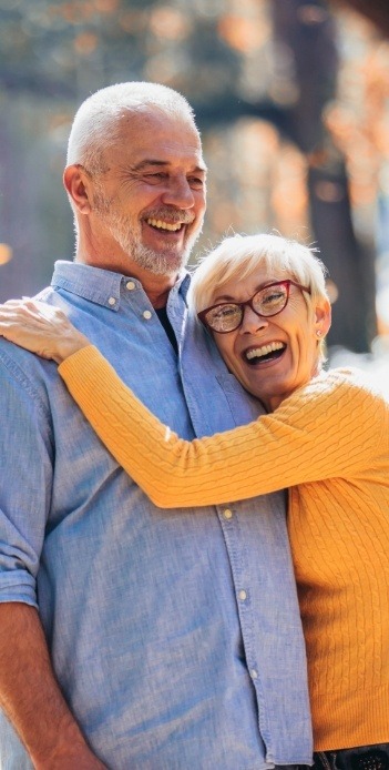 Senior woman in yellow sweater hugging senior man in denim shirt