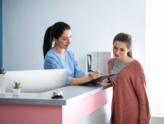 Dental team member at front desk showing a clipboard to a patient