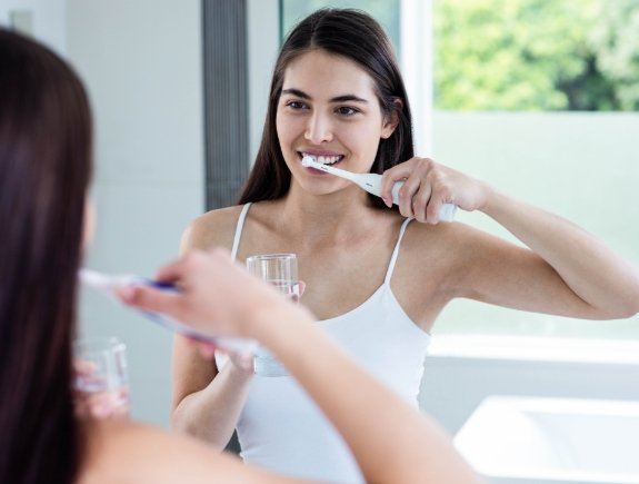 Woman brushing her teeth in front of bathroom mirror