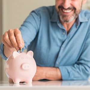 Smiling man putting money into a piggy bank