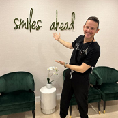Doctor Magid gesturing to sign on wall that says smiles ahead
