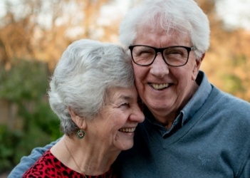 Elderly man and woman smiling and holding each other outdoors