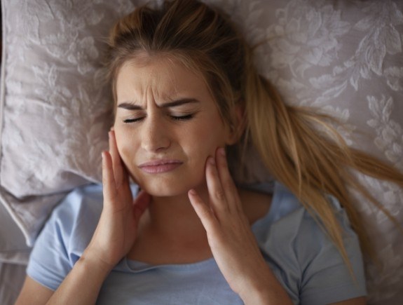 Woman lying in pain holding both side of her jaw in pain