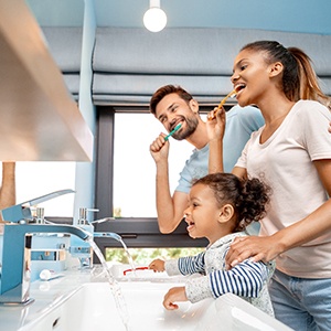 Man, woman, and girl brushing teeth together in bathroom