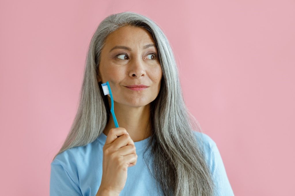 Woman with grey hair smiling while holding toothbrush