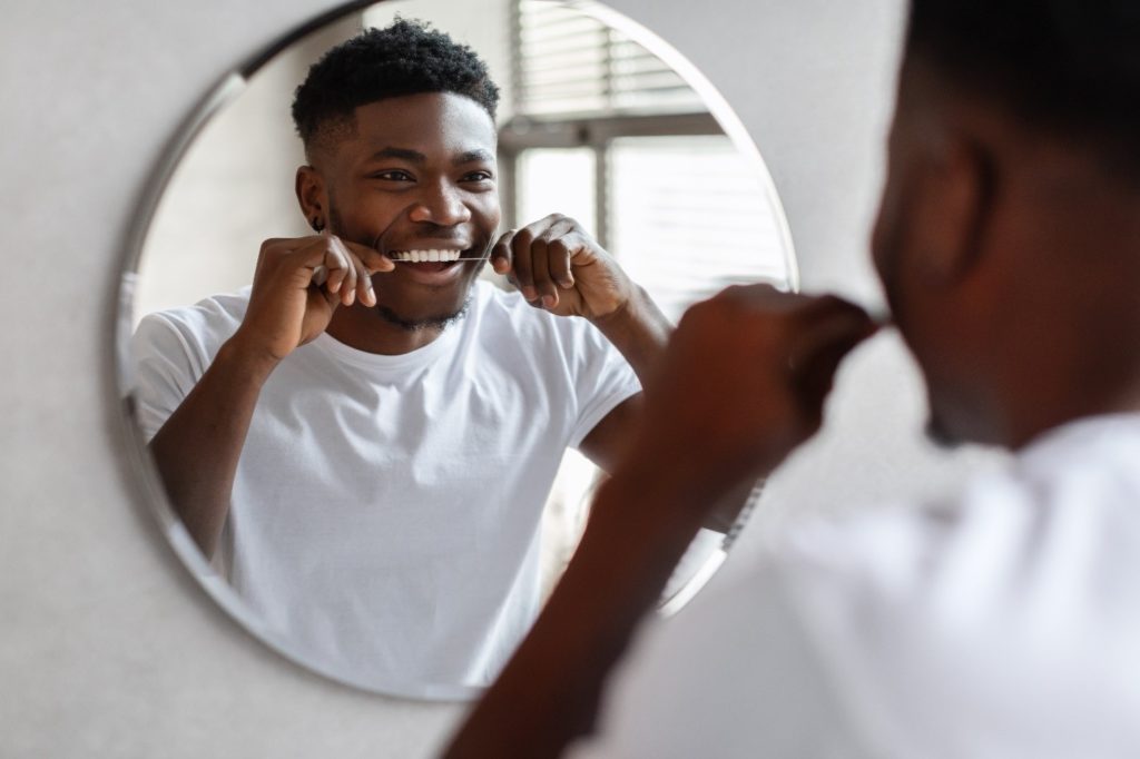 Male smiling while brushing his teeth in bathroom