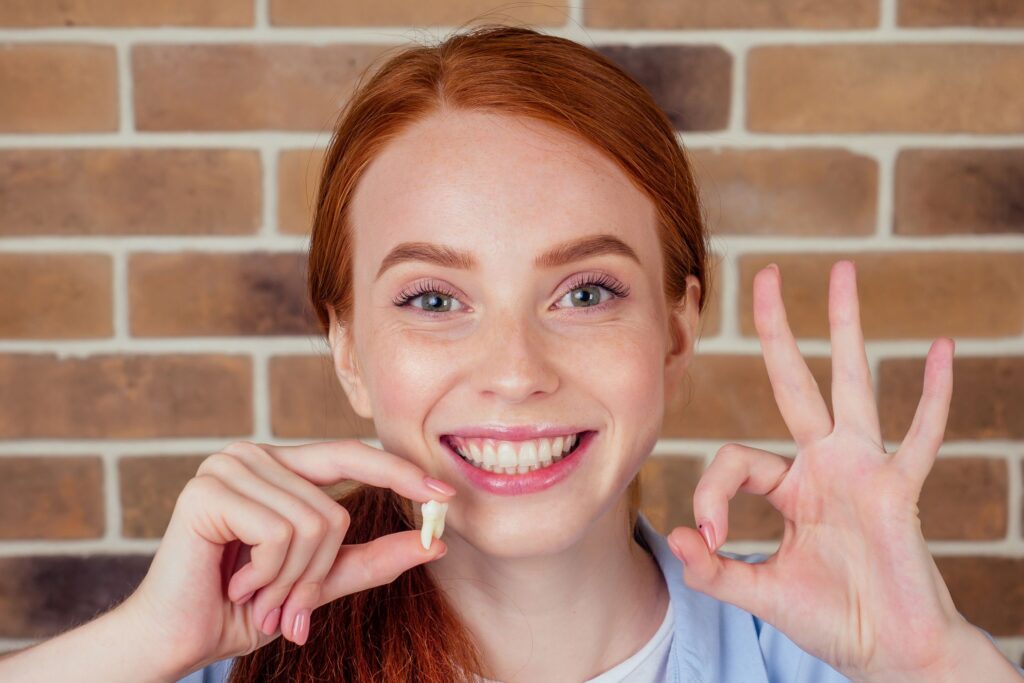 Woman making "ok" sign with one hand holding extracted tooth in the other