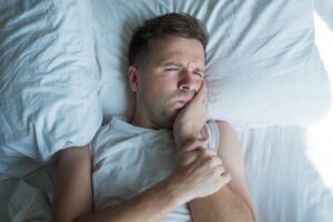 Man lying in bed holding jaw in pain.
